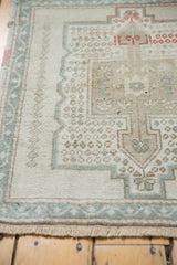 Distressed ivory Oushak rug, showing seafoam green meandering vine border and textured pile.