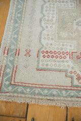 Corner detail of distressed vintage Oushak rug, showing ivory field, seafoam border, and rose fringe.