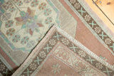 Distressed Oushak rug corner showing low pile, pale copper, and mint green border motifs.