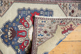Folded Vintage Oushak rug displaying blue floral medallion, beige ground, and original selvage.