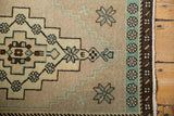 Distressed Oushak rug corner with beige geometric field, mint green border, and original side selvage.