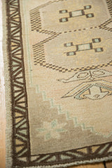 Distressed texture of Oushak rug's geometric border and muted ivory, brown, seafoam patterns.