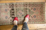 Vintage distressed Oushak rug with abrashed field, faded geometric diamond motifs, and blush rose colors.