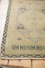 Distressed Oushak rug mat corner, textured beige pile, charcoal black geometric border, and fringe.