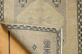 Distressed Oushak rug corner, revealing worn beige pile and painted number on hand-knotted reverse.