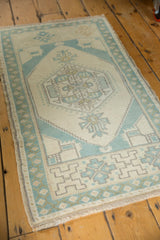 Distressed Oushak rug detail, showing muted mint green-blue geometric border and ivory field.
