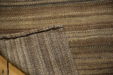 Curled corner of vintage Moroccan Kilim rug, revealing hand-woven brown striped texture.