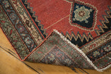 Karabagh runner corner lifted, revealing madder red field, worn pile, and hand-knotted construction.