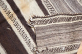 Folded Moroccan Kilim rug showing natural ivory and dark brown textured alternating stripes.
