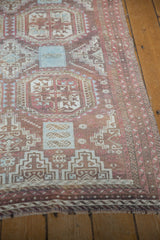 Distressed vintage Belouch rug corner, showcasing faded geometric patterns and worn fringe.