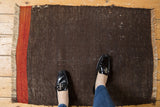 Corner of a hand woven Turkish Kilim rug, with brick red geometric stripe on charcoal.