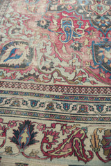 Distressed antique Khorassan carpet close-up, featuring ivory, fuscia, and navy floral with pawn border.