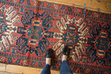Person's feet on vintage Karaja runner with brick red, navy, and ivory geometric medallions.