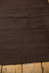 Dark chocolate brown Kilim rug showing visible warp, wefting, and secure edge.