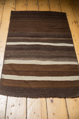 Hand woven Turkish Kilim runner's secured end, showing striated coffee, chocolate, and ivory bands.
