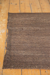 Hand-woven coffee brown Kilim rug with natural striations and secure side edge.
