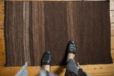 A person's feet on a vintage Turkish Kilim runner with brown and ivory abrashes.