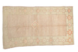 Distressed vintage Oushak rug: pale blush field, central stepped medallion, celadon geometric star border.
