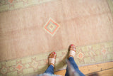 Distressed Oushak carpet's worn low pile, with pale blush and geometric celadon patterns.