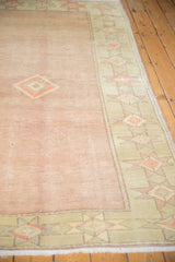 Geometric seafoam and cantaloupe starburst border on distressed pale blush Oushak rug with low pile.