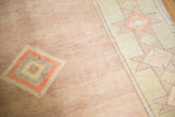 Vintage distressed Oushak carpet showing low pile texture, pale blush field, geometric motif, and antique ivory border.