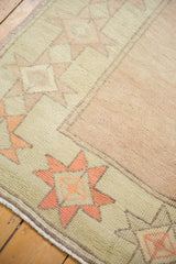Vintage distressed Oushak rug corner showcasing cantaloupe starbursts on a pale celadon border.