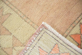 Distressed Oushak rug corner shows hand-knotted low pile, secured sides, white fringe, and pale blush.