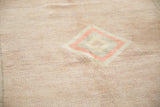 Low pile distressed Oushak carpet with pale blush, ivory, and green geometric motif.