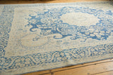 Whimsical blue floral wreathe and vinery on a distressed antique ivory Kerman carpet.