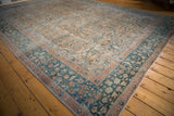 Distressed vintage Tabriz carpet shows teal indigo border with blush floral motifs on a worn sand field.