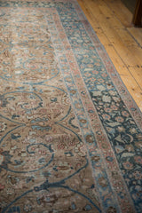Distressed Tabriz carpet close-up: beige field, blue arabesques, blush florals, faint foundation.