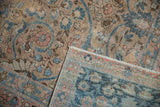 Folded vintage distressed Tabriz carpet showing worn pile, teal indigo, blush, and sand floral arabesques.
