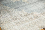 Distressed Oushak rug corner showing ivory border with scrolling vinery and pale denim blue field.