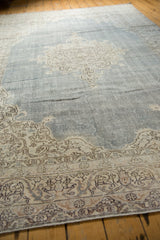 Distressed Oushak rug detail: pale denim blue field, ornate beige scrolling vinery, visible wear.