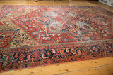 Vintage Heriz carpet corner with navy border, floral motifs, and field's isolated wear.