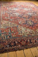 Vintage Heriz rug corner detail: cherry red field, geometric border, and splayed blue floral motifs.