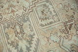 Distressed Heriz carpet showing serrated rectilinear patterns in muted sand, coffee, and blue-green.