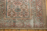 Distressed corner of a vintage Hamadan rug, showing blush field, geometric borders, exposed foundation.