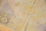 Distressed vintage Oushak rug's pile, showing faded saffron yellow, lavender, and visible wear.