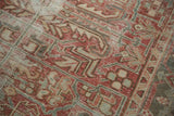 Distressed Heriz carpet showing faded cranberry and dusty gold rectilinear patterns with visible foundation.