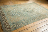Distressed Malayer carpet corner, showing dark brown border and faded teal, ivory, gold geometric field.