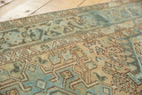 Distressed vintage Karaja runner close-up, geometric pattern in muted teal and dusty gold tones.