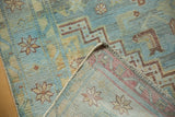 Corner of distressed Malayer rug, showing abrash texture, pale blue and saffron geometric motifs, and hand-knotted back.