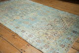 Vintage distressed Malayer rug corner showing pale blue field, saffron florals, zigzag border, and fringe.