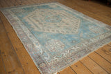 Distressed Afshar rug corner, aqua blue and sand geometric field with low pile and visible foundation.