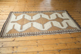 Angled view of hand-knotted Gabbeh rug with geometric ivory, charcoal, copper brown, diamond border.