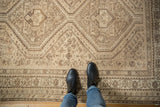 Geometric medallions and floral patterns on distressed vintage Shiraz rug in time-softened beige, brown.