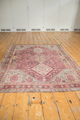 Perspective view of a vintage Qashqai rug showing its distressed texture and geometric medallions in fuchsia and sky blue.