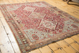 A vintage distressed Qashqai rug with intricate geometric medallions in fuchsia and sky blue.