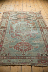 Distressed Malayer rug corner with fringed end, muted sea foam green, raspberry, and ivory geometric patterns.